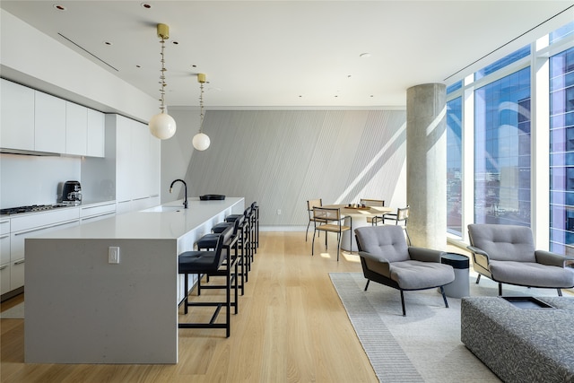 kitchen with light wood-type flooring, a kitchen island with sink, white cabinetry, and decorative light fixtures