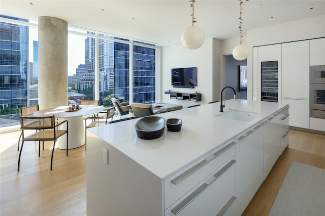 kitchen featuring sink, white cabinets, light hardwood / wood-style flooring, a center island with sink, and decorative light fixtures