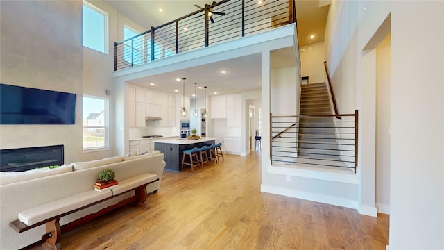 living room with light wood-type flooring, a towering ceiling, and a tiled fireplace