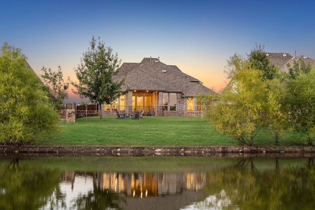 back house at dusk featuring a water view and a yard