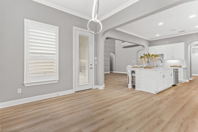 kitchen with ornamental molding, light hardwood / wood-style flooring, an island with sink, and white cabinets