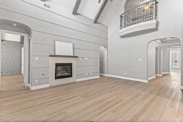 unfurnished living room with wood walls, light wood-type flooring, a tiled fireplace, and a high ceiling