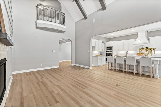 living room with high vaulted ceiling, light wood-type flooring, and beam ceiling