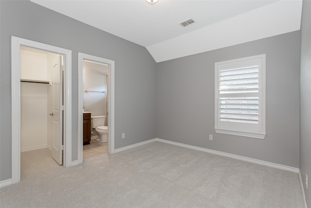 unfurnished bedroom with a spacious closet, a closet, lofted ceiling, ensuite bathroom, and light colored carpet