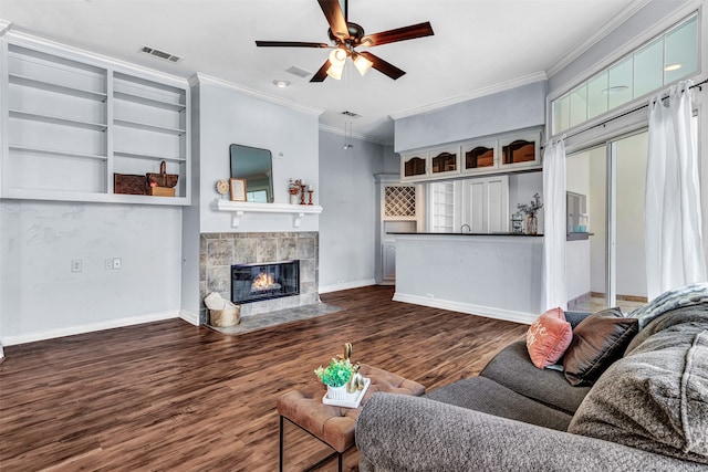 living room featuring built in shelves, a fireplace, crown molding, dark hardwood / wood-style flooring, and ceiling fan