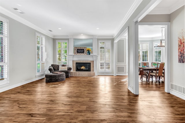 living room featuring dark hardwood / wood-style flooring, a tile fireplace, ornamental molding, and plenty of natural light