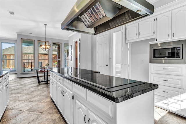 kitchen featuring black electric cooktop, stainless steel microwave, wall chimney range hood, a kitchen island, and white cabinetry