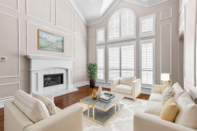 living room featuring wood-type flooring, ornamental molding, a tiled fireplace, and high vaulted ceiling