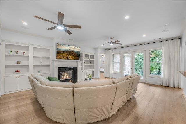 living room with ornamental molding, built in shelves, light hardwood / wood-style floors, and ceiling fan