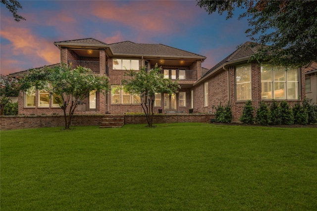 back house at dusk with a lawn and a balcony