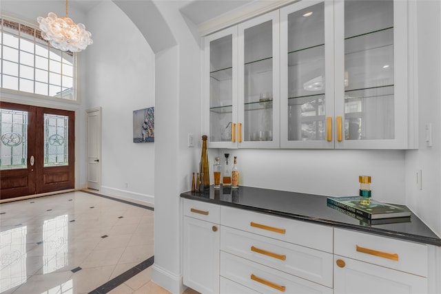 bar with light tile patterned floors, decorative light fixtures, white cabinetry, a high ceiling, and a notable chandelier