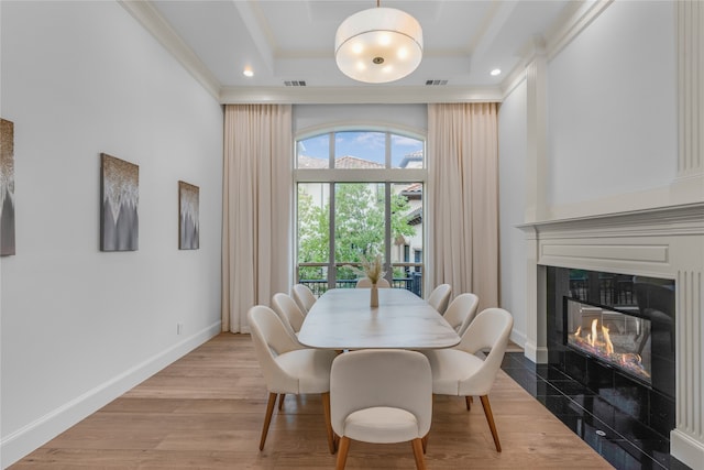 dining room featuring a tray ceiling, a fireplace, hardwood / wood-style floors, and crown molding