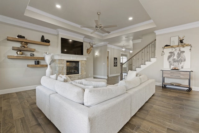 living room with a stone fireplace, dark hardwood / wood-style floors, crown molding, a tray ceiling, and ceiling fan