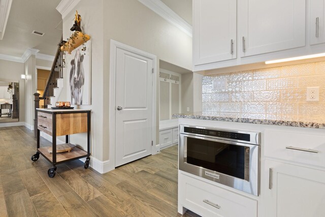 135 Valley Vw, Glen Rose, TX 76043 - kitchen featuring ornamental molding, oven, white cabinetry, light wood-style flooring, and light stone counters