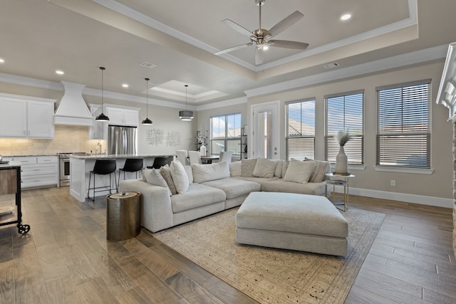 living room with ornamental molding, light hardwood / wood-style flooring, ceiling fan, and a tray ceiling