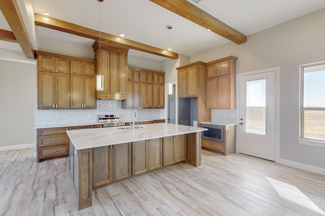 kitchen featuring tasteful backsplash, sink, pendant lighting, a center island with sink, and beamed ceiling