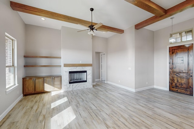 unfurnished living room with a premium fireplace, beamed ceiling, light hardwood / wood-style floors, and ceiling fan with notable chandelier