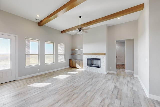 unfurnished living room featuring beamed ceiling, light hardwood / wood-style floors, ceiling fan, and a high end fireplace