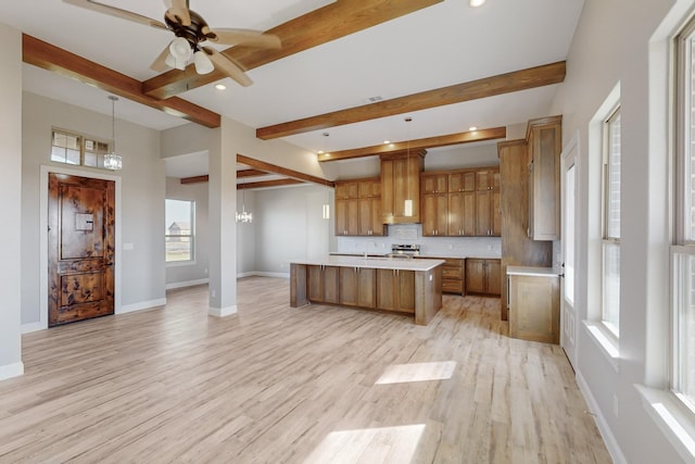 kitchen featuring beam ceiling, light wood-type flooring, a kitchen island with sink, and hanging light fixtures