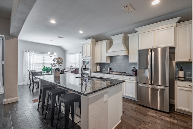 kitchen with custom exhaust hood, stainless steel appliances, dark hardwood / wood-style floors, and an island with sink