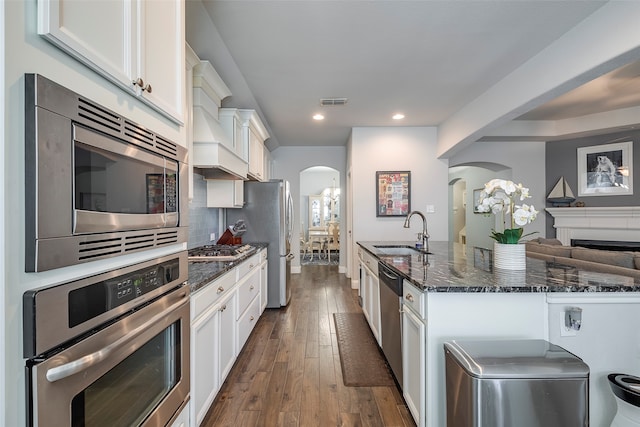 kitchen with appliances with stainless steel finishes, dark stone countertops, white cabinets, dark hardwood / wood-style floors, and sink