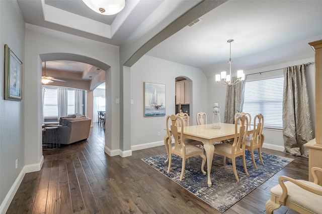 dining room featuring ceiling fan with notable chandelier, a tray ceiling, and dark hardwood / wood-style floors