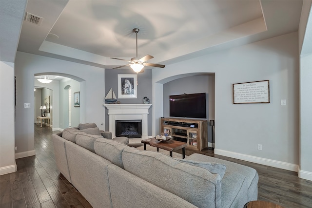 living room featuring a raised ceiling, dark hardwood / wood-style floors, and ceiling fan