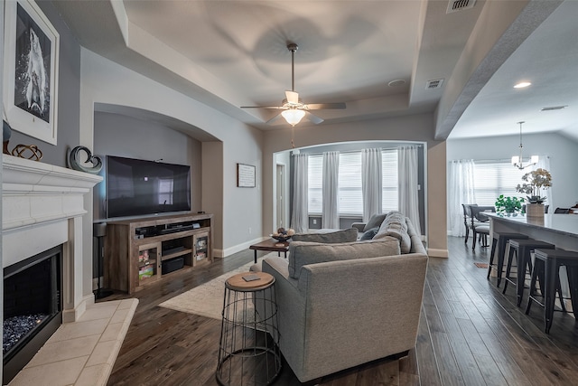 living room with ceiling fan with notable chandelier, a tile fireplace, and dark hardwood / wood-style floors