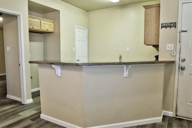 kitchen with dark wood-type flooring, baseboards, a breakfast bar, dark stone counters, and a peninsula