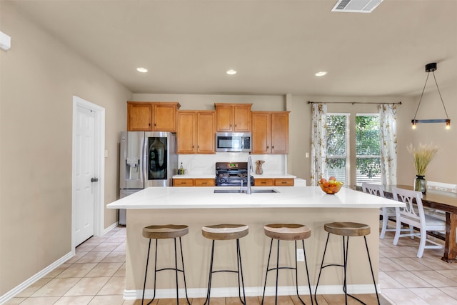 kitchen with appliances with stainless steel finishes, a center island with sink, a breakfast bar area, and light tile patterned flooring