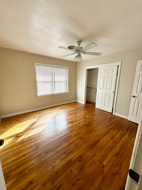 unfurnished bedroom with a textured ceiling, wood-type flooring, ceiling fan, and a closet