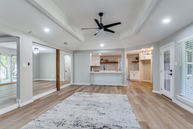 living room featuring ornamental molding, ceiling fan with notable chandelier, light hardwood / wood-style floors, and a tray ceiling