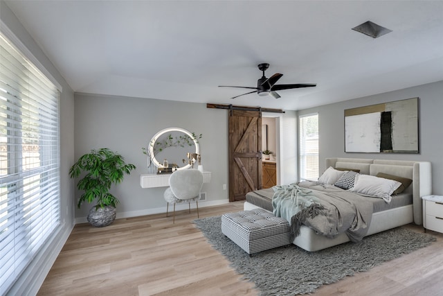 bedroom with ceiling fan, light hardwood / wood-style flooring, and a barn door