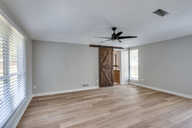 unfurnished room featuring a barn door, light hardwood / wood-style floors, and ceiling fan