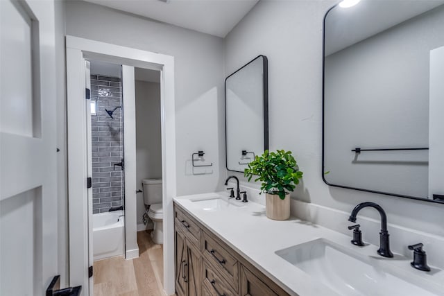 full bathroom with tiled shower / bath combo, vanity, hardwood / wood-style floors, and toilet