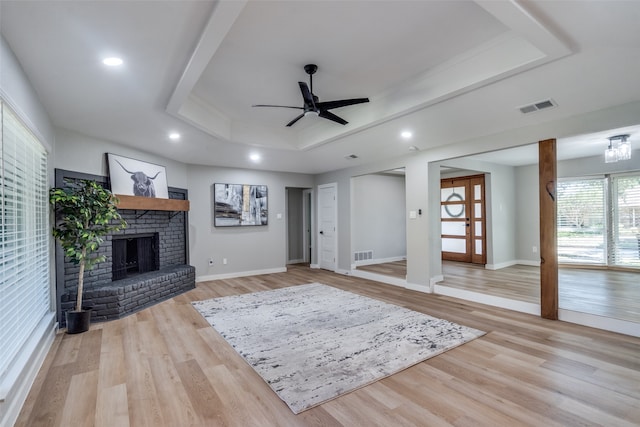 unfurnished living room featuring a brick fireplace, light wood-type flooring, ceiling fan, and a raised ceiling