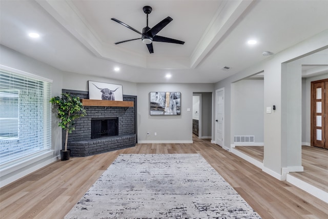 living room featuring light hardwood / wood-style flooring, ceiling fan, a raised ceiling, and a fireplace