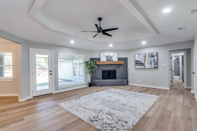 living room with a raised ceiling, light hardwood / wood-style floors, ceiling fan, and a brick fireplace