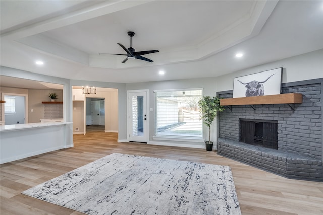 unfurnished living room with light hardwood / wood-style floors, a fireplace, a tray ceiling, and a wealth of natural light