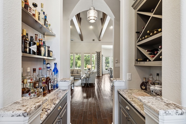 bar featuring gray cabinets, light stone counters, beam ceiling, hanging light fixtures, and dark hardwood / wood-style flooring