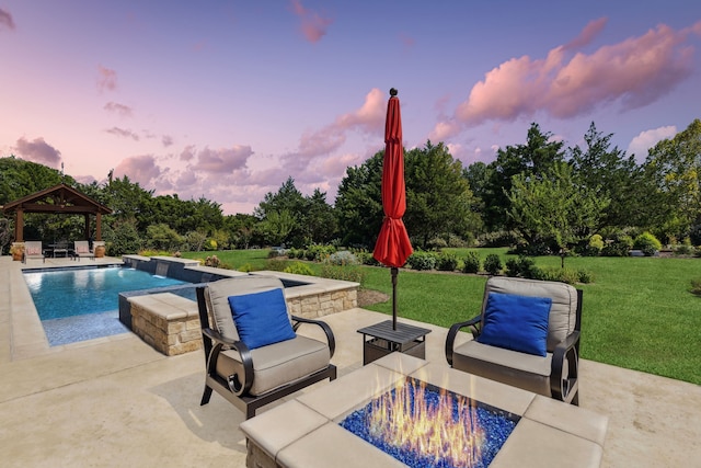 pool at dusk featuring a gazebo, a patio area, a fire pit, and a lawn