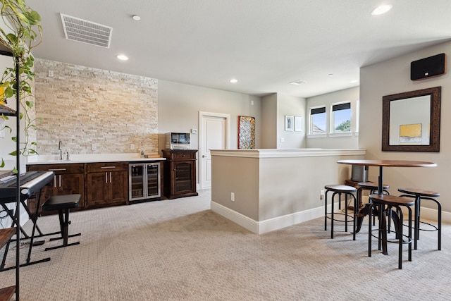 bar featuring dark brown cabinets, beverage cooler, and light colored carpet