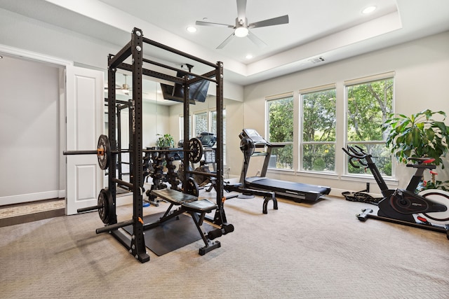 exercise room with ceiling fan, a raised ceiling, and carpet flooring