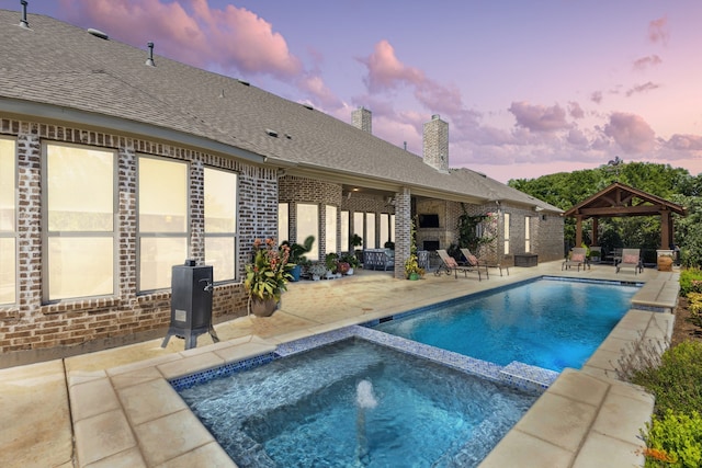 pool at dusk with an in ground hot tub, a patio area, and a gazebo