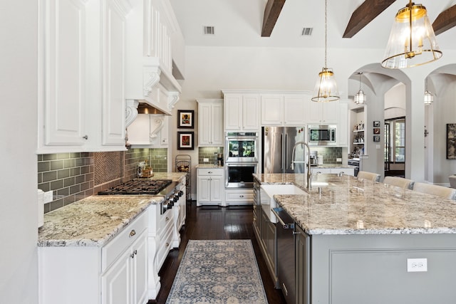 kitchen with appliances with stainless steel finishes, a center island with sink, white cabinetry, and pendant lighting