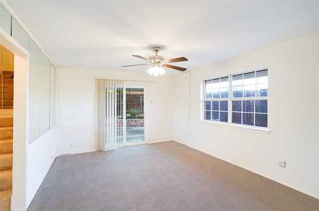 carpeted spare room with ceiling fan and stairs