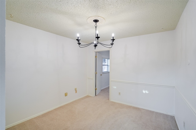 spare room featuring a textured ceiling, light colored carpet, and an inviting chandelier