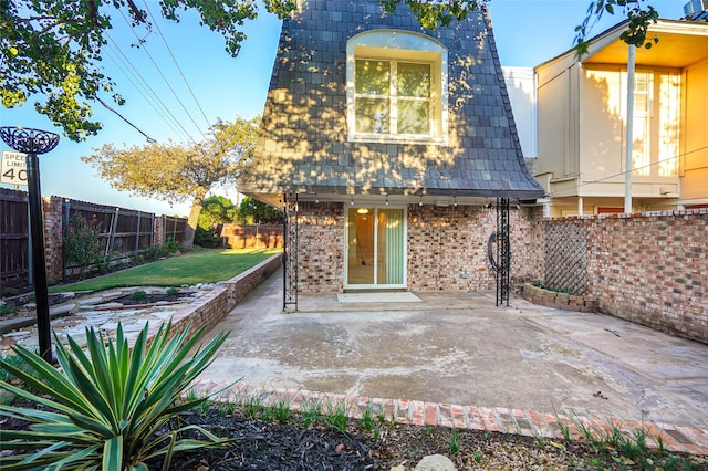 view of front of home featuring a front yard, a patio area, a fenced backyard, and mansard roof