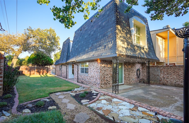 rear view of property with brick siding, mansard roof, a patio, and a yard