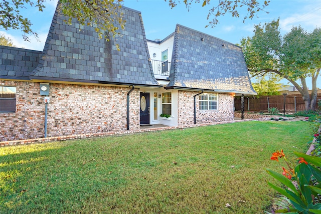 rear view of property featuring brick siding, a yard, mansard roof, fence, and a balcony